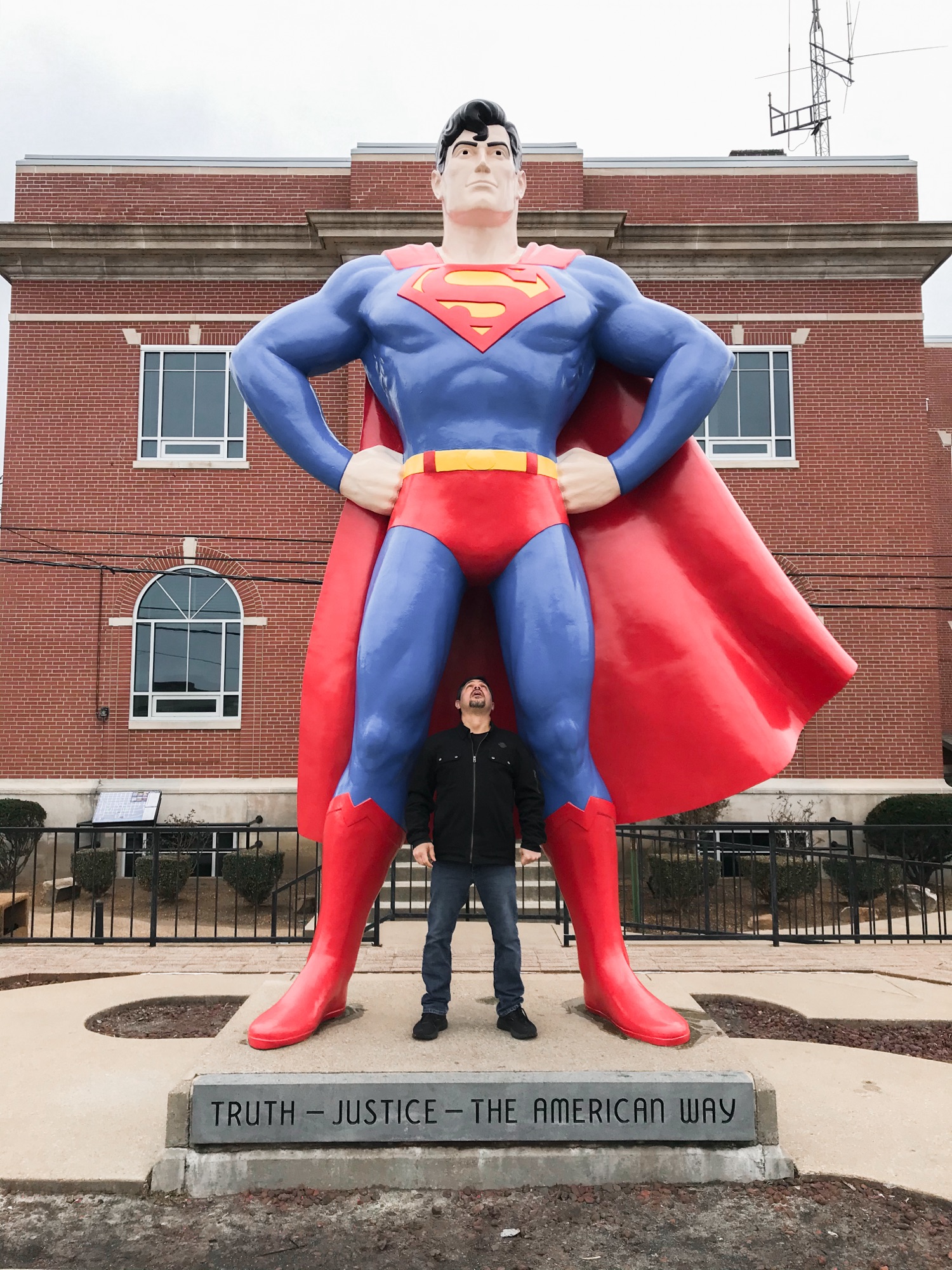 The photo on the left is Dominic looking up at a 15 ft. Superman statue. The statue has a plaque on the front that states, "Truth-Justice-The American Way". The photo on the right is Angela inside a Superman telephone booth at the Superman Museum.