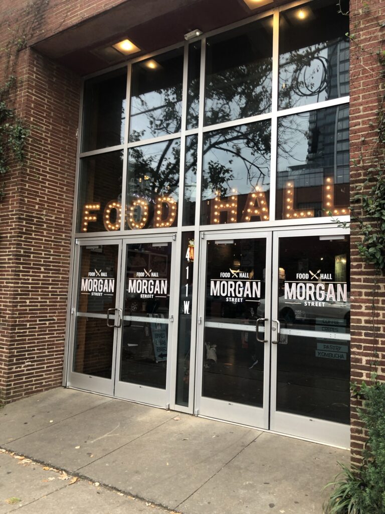 The doorway to Morgan Street Food Hall. "Food Hall" is lit up on the glass window.