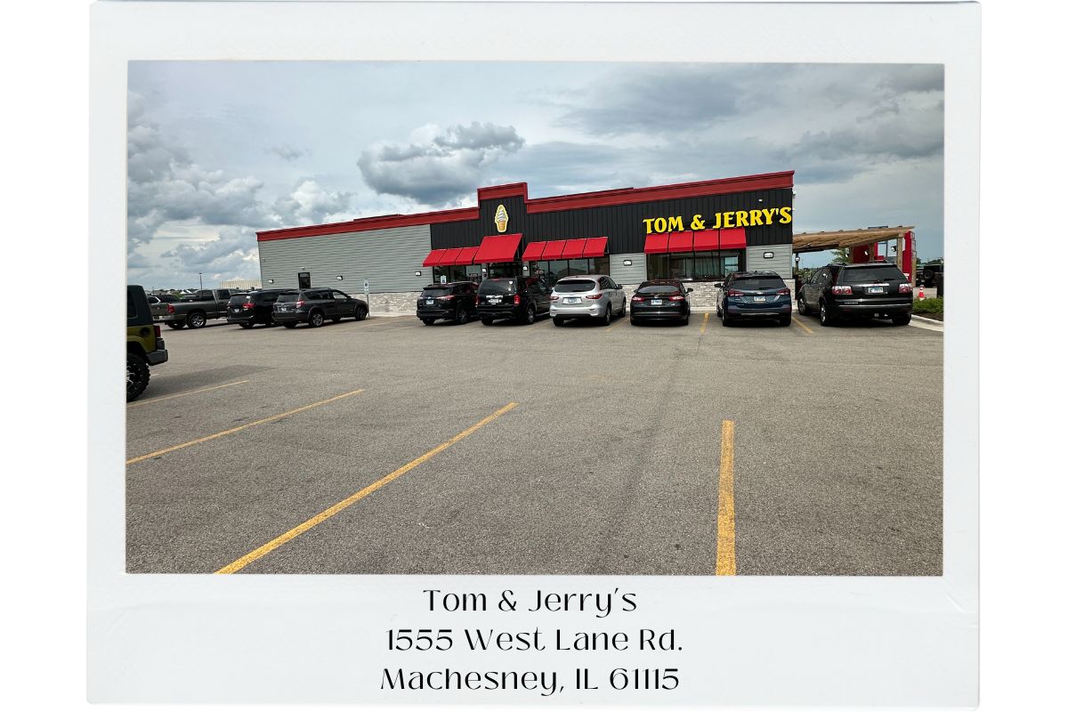 Polaroid style picture of the outside of Tom & Jerry's restaurant with the name and address noted on the bottom of the picture. It's a gray and black building with red awnings. There are a number of cars parked in front of the restaurant.