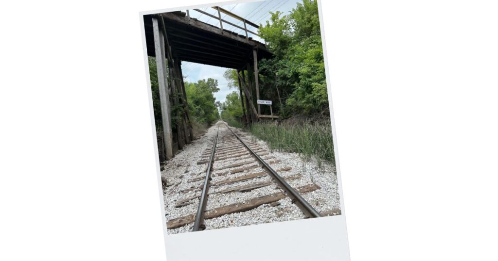 Picture of railroad tracks that lead under a tall bridge.