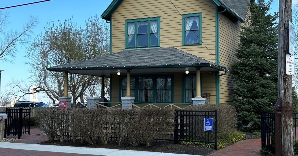 A Christmas Story house. It's a yellow house with green windows and a leg lamp in the window. There are brown bushes in front.