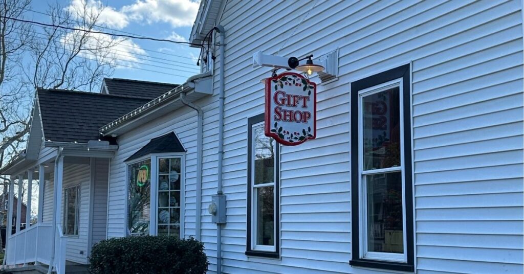 White sided building with a "Gift Shop" sign hanging from the side of the building. This is the gift shop at A Christmas Story house.