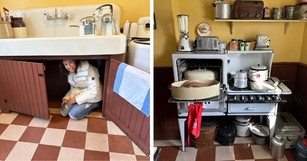 A Christmas Story house- kitchen. The image shows two scenes from a vintage kitchen. On the left, I am wearing a white winter jacket and crouching inside a cabinet beneath a large farmhouse-style sink with retro kitchen appliances and jars on the counter. The cabinet doors are open, and the checkered floor adds to the retro feel. On the right, there is an antique stove with a turkey in a roasting pan in the oven, and various vintage kitchen items such as a blender, toaster, and coffee percolator are displayed on top. Shelves above hold old-fashioned containers and a radio.